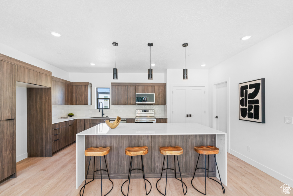 Kitchen with appliances with stainless steel finishes, modern cabinets, light wood-type flooring, light countertops, and decorative backsplash