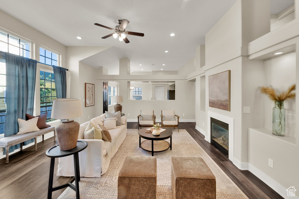 Living area with dark wood-style flooring, a glass covered fireplace, ceiling fan, baseboards, and recessed lighting