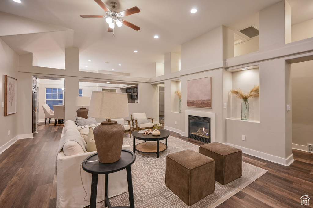 Living area featuring a glass covered fireplace, dark wood-style flooring, a ceiling fan, recessed lighting, and baseboards