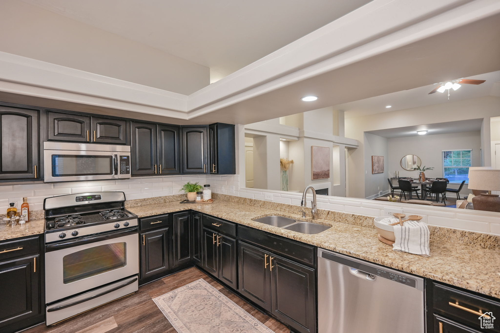 Kitchen featuring stainless steel appliances, a sink, wood finished floors, light stone counters, and backsplash