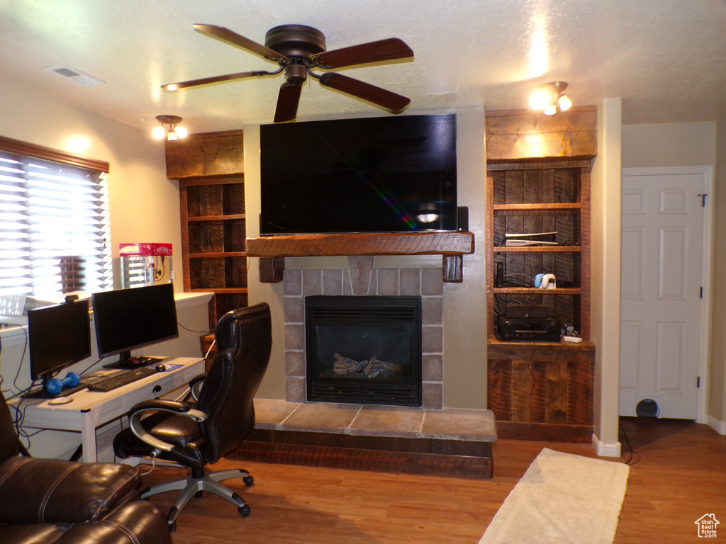Office with ceiling fan, a tiled fireplace, and wood finished floors