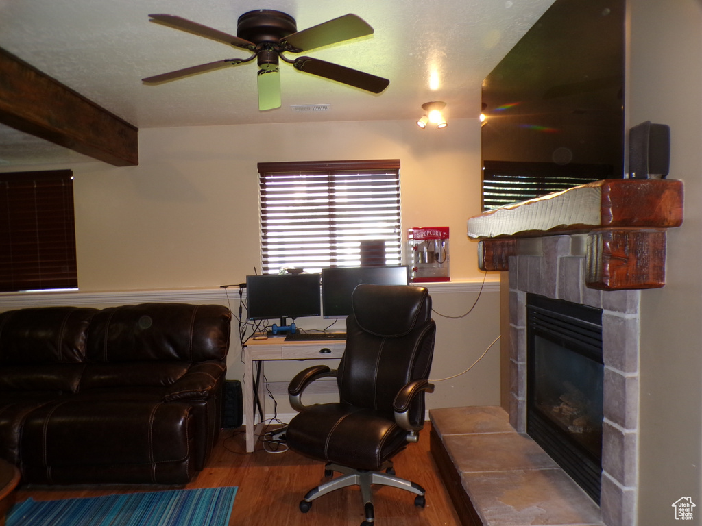 Office area featuring wood finished floors, a fireplace, ceiling fan, and beamed ceiling