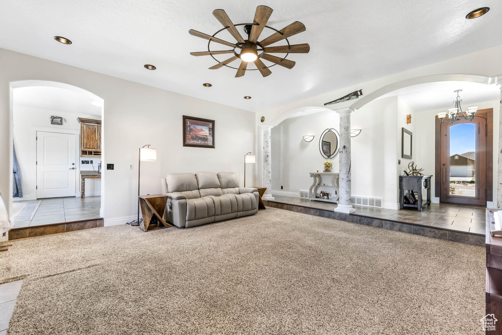 Living area with arched walkways, ceiling fan, decorative columns, carpet, and baseboards