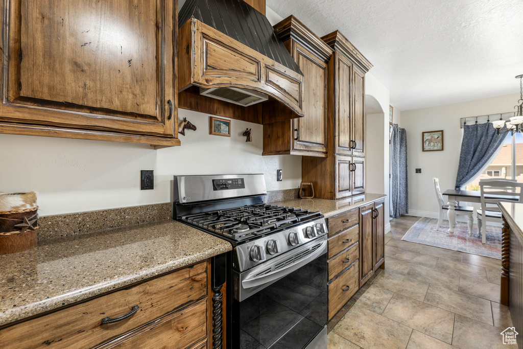 Kitchen featuring gas range, custom range hood, a chandelier, light stone counters, and arched walkways