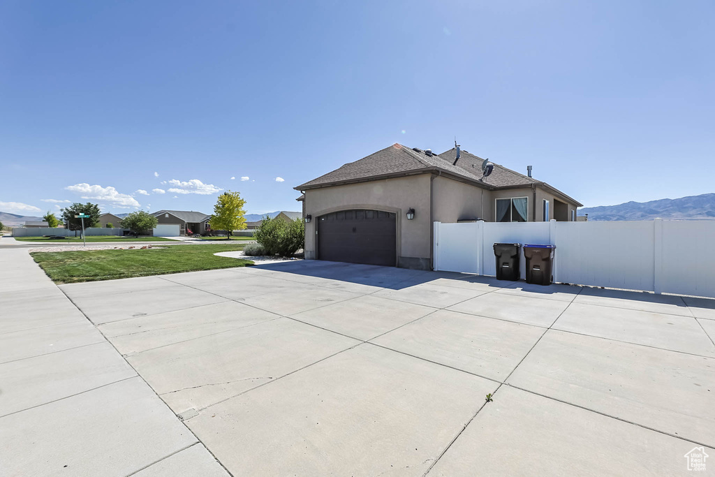 View of side of home with stucco siding, concrete driveway, an attached garage, and roof with shingles