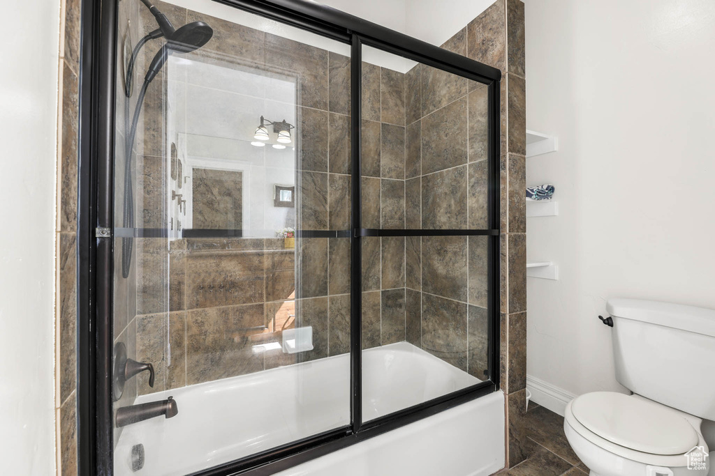 Bathroom featuring toilet, baseboards, and shower / bath combination with glass door