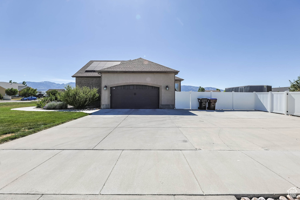 View of side of home featuring solar panels, driveway, a garage, stucco siding, and a mountain view