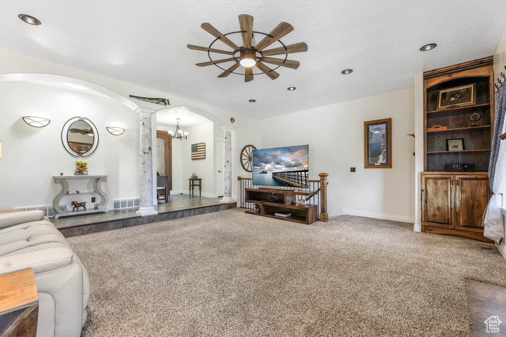 Carpeted living area with ornate columns, arched walkways, a ceiling fan, a chandelier, and baseboards