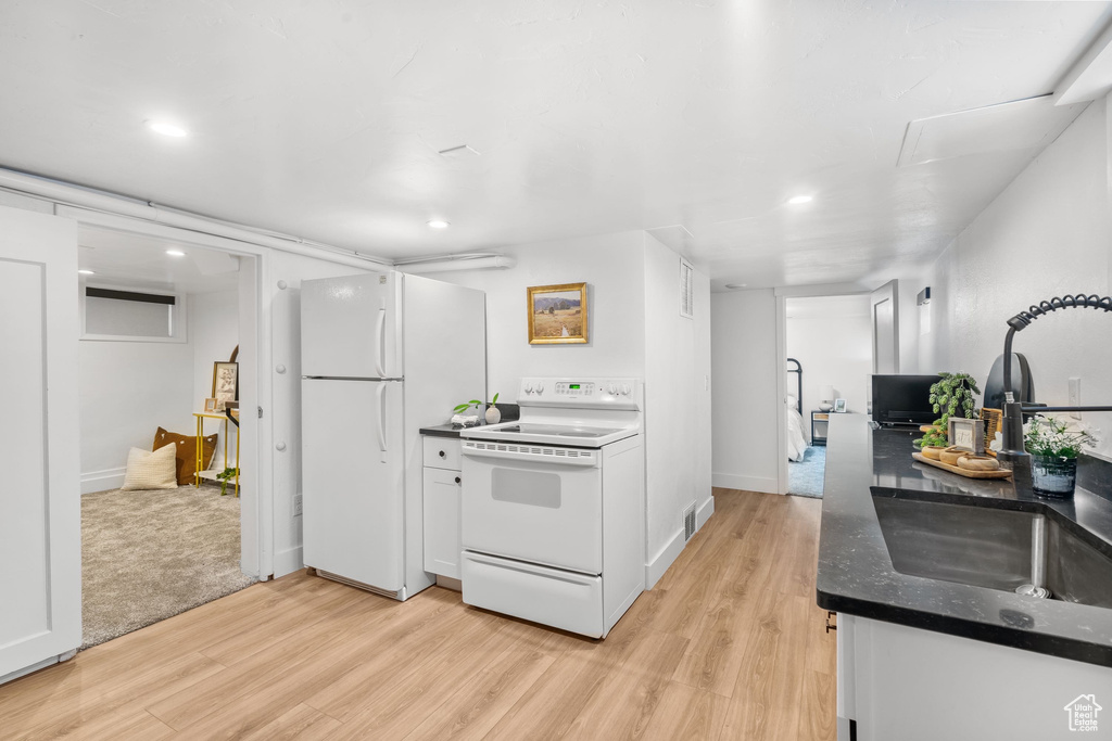 Kitchen featuring white appliances, light wood-type flooring, a sink, dark countertops, and recessed lighting