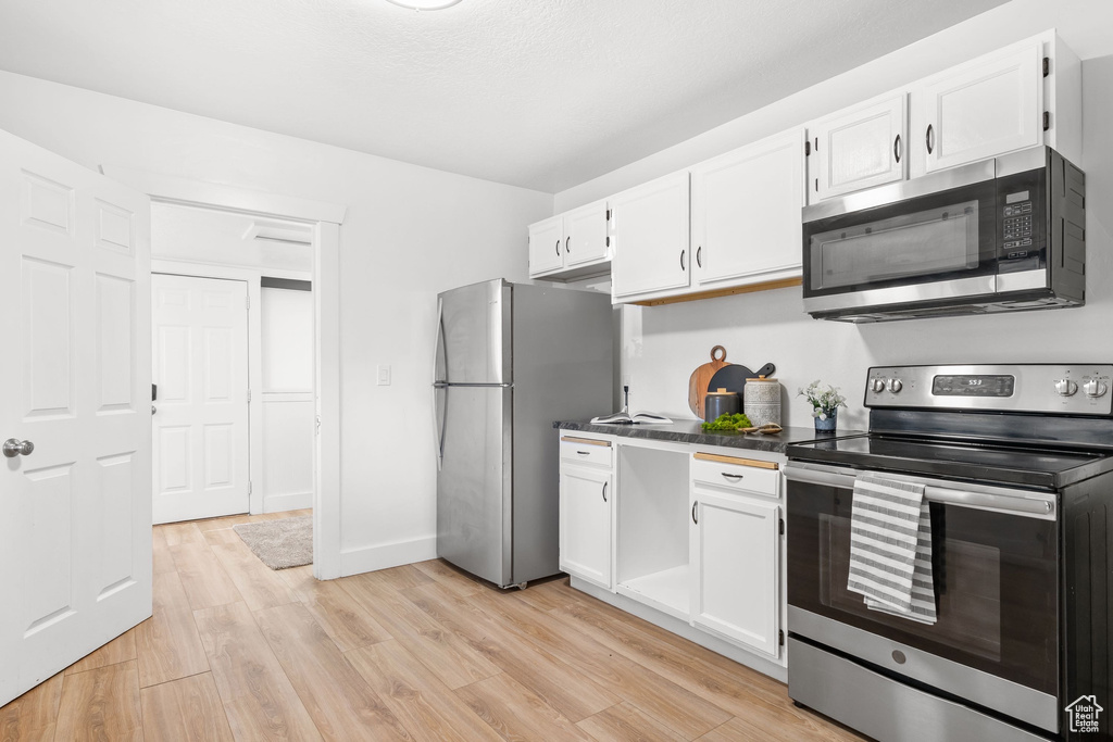 Kitchen featuring appliances with stainless steel finishes, white cabinets, light wood-style floors, and dark countertops