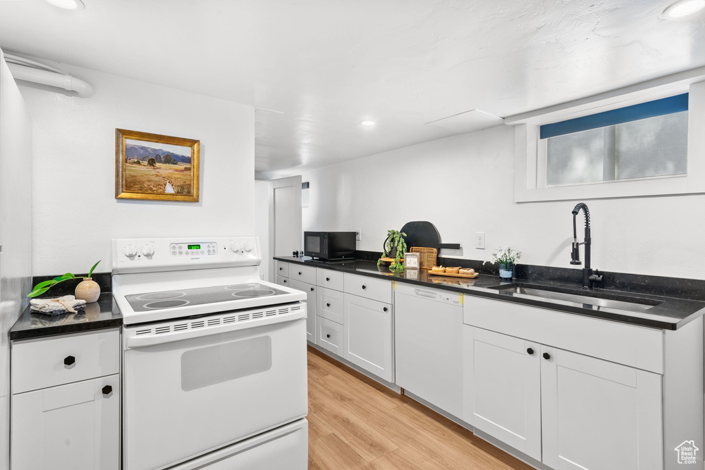 Kitchen with white appliances, a sink, dark countertops, light wood-type flooring, and recessed lighting