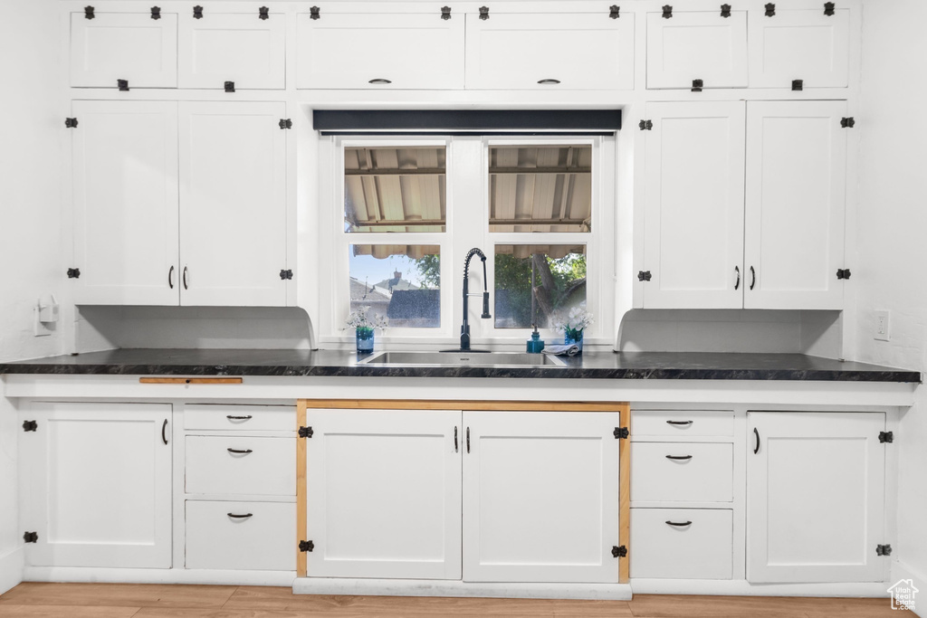 Kitchen with a sink, white cabinetry, dark stone countertops, and light wood-style flooring