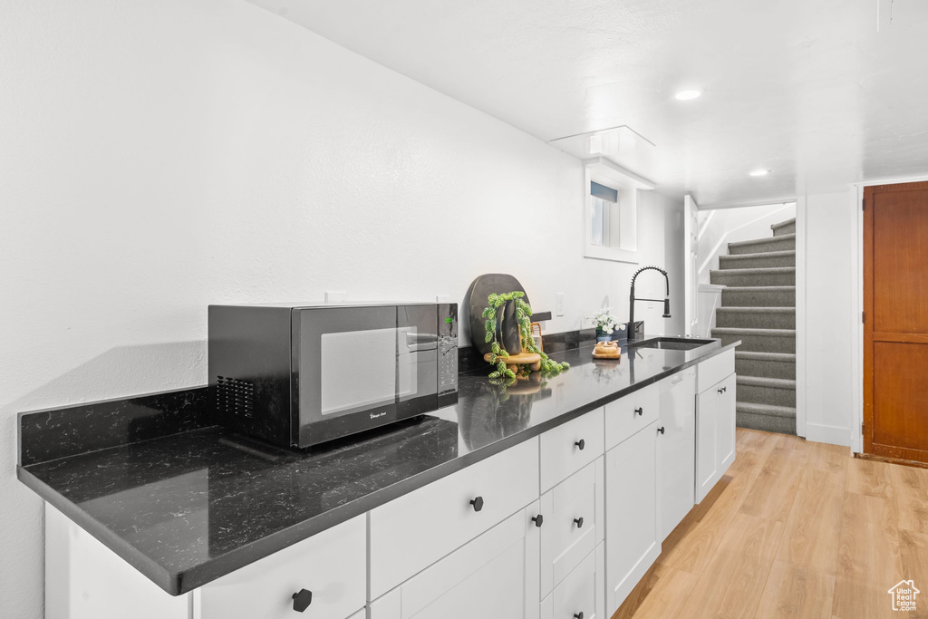 Kitchen with a sink, black microwave, light wood-style floors, white cabinetry, and dark stone countertops