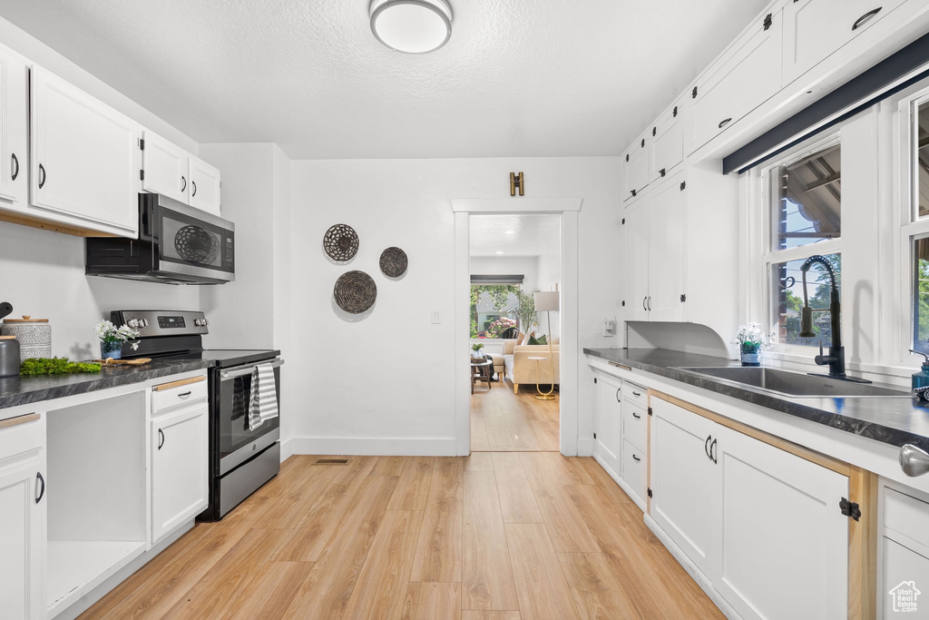 Kitchen featuring appliances with stainless steel finishes, a sink, light wood-style floors, white cabinetry, and dark countertops