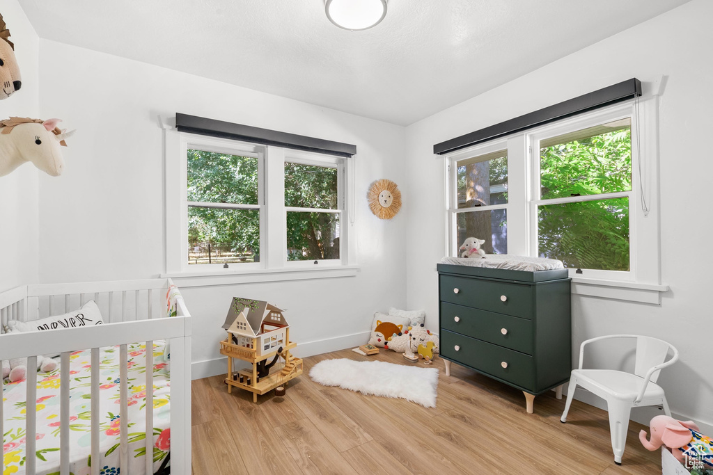 Bedroom with wood finished floors, a crib, and baseboards