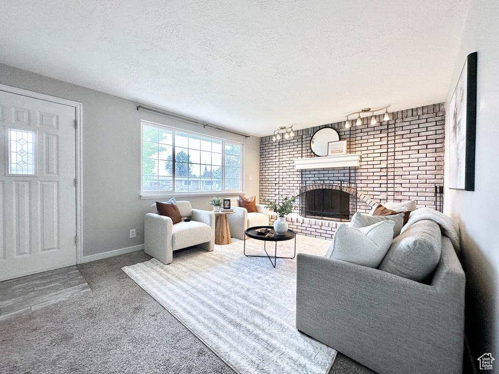 Living area with a brick fireplace, carpet flooring, a textured ceiling, baseboards, and brick wall