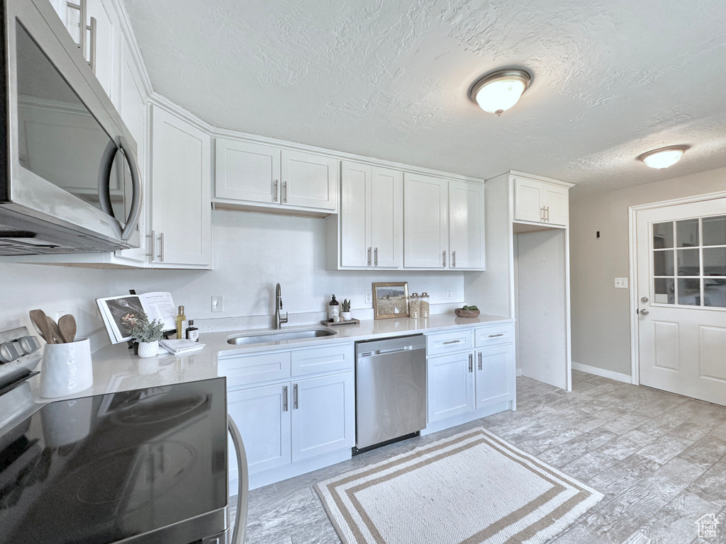 Kitchen with stainless steel appliances, a sink, light countertops, white cabinetry, and a textured ceiling