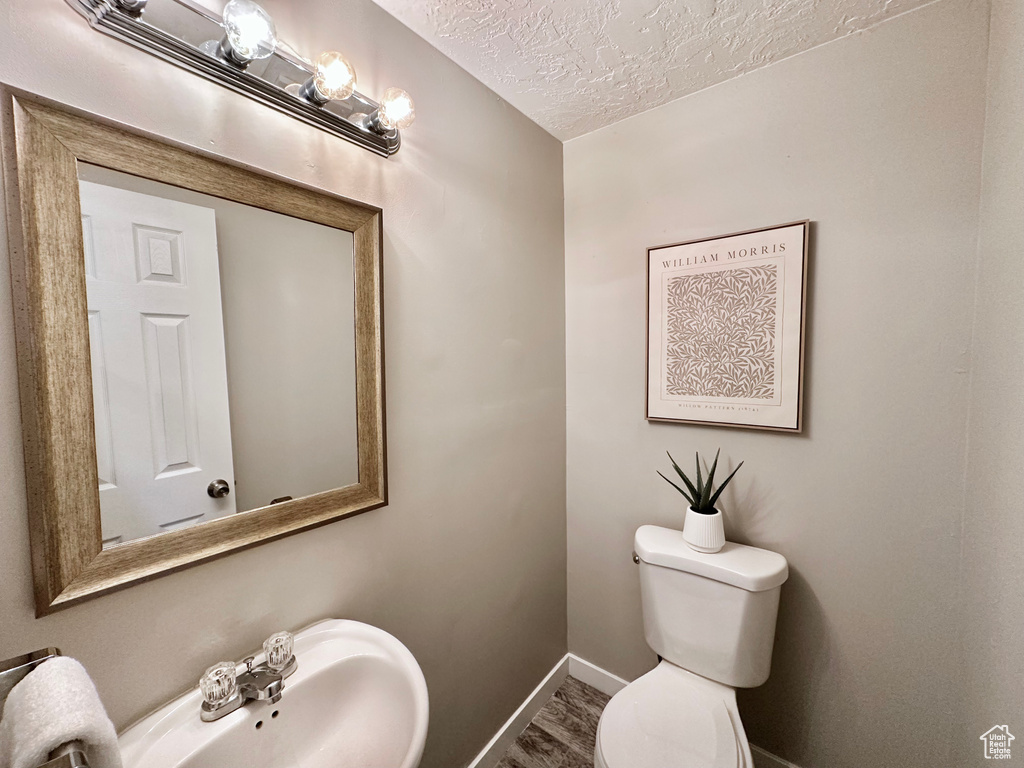 Bathroom with toilet, a textured ceiling, baseboards, and wood finished floors