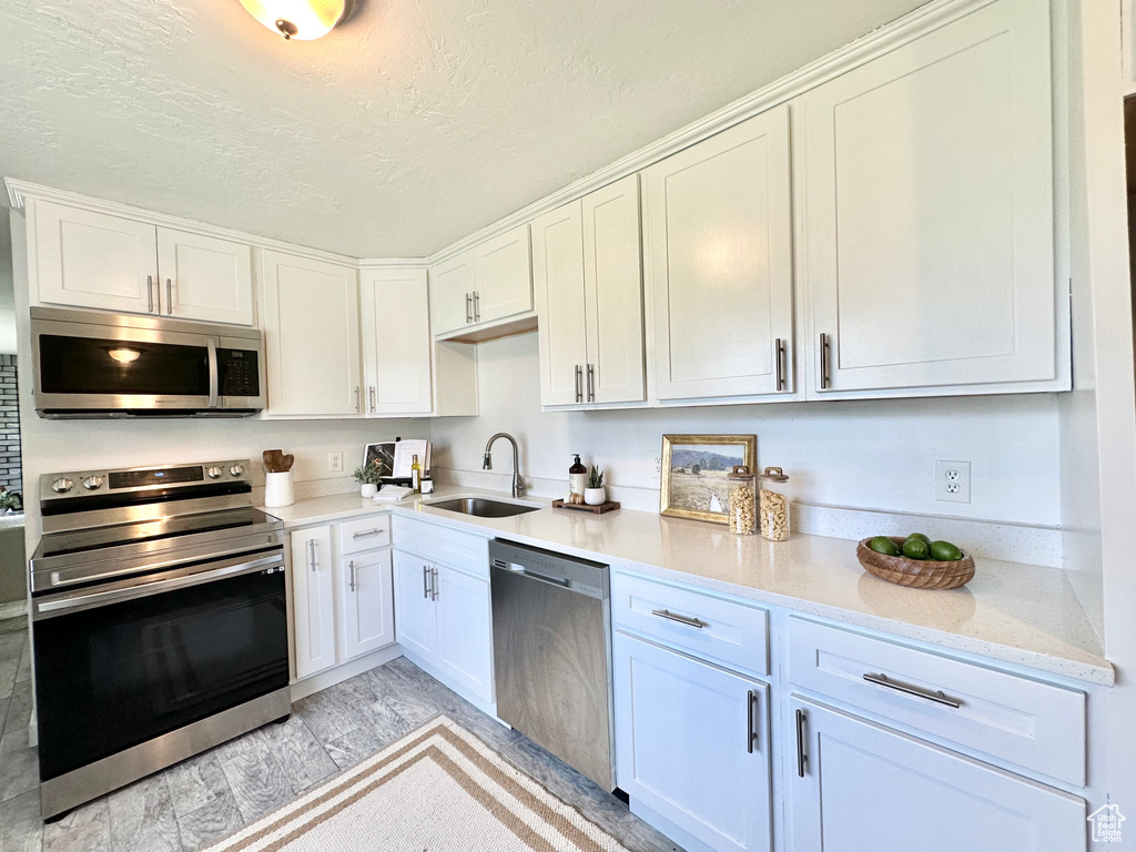 Kitchen featuring appliances with stainless steel finishes, a sink, white cabinets, light wood-type flooring, and a textured ceiling