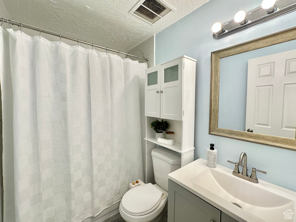 Full bath with a textured ceiling, toilet, vanity, and a shower with shower curtain