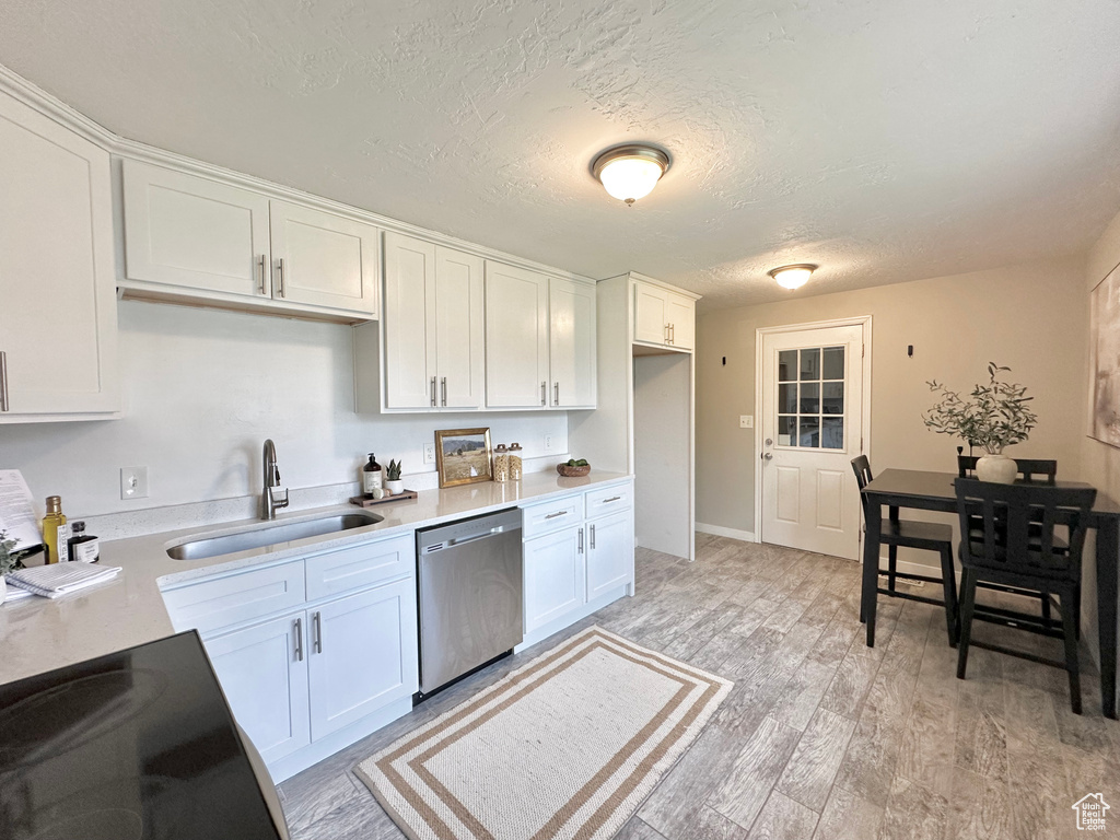 Kitchen featuring a sink, stainless steel dishwasher, white cabinets, a textured ceiling, and light countertops