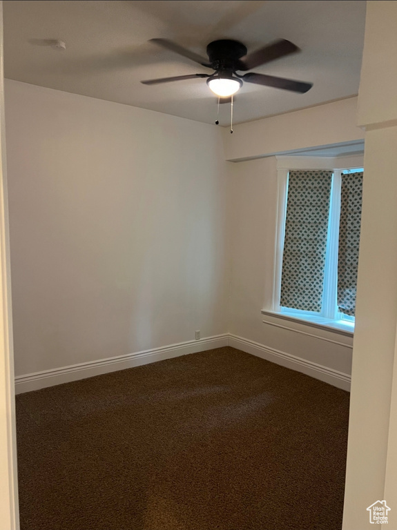 Spare room with dark colored carpet, ceiling fan, and baseboards
