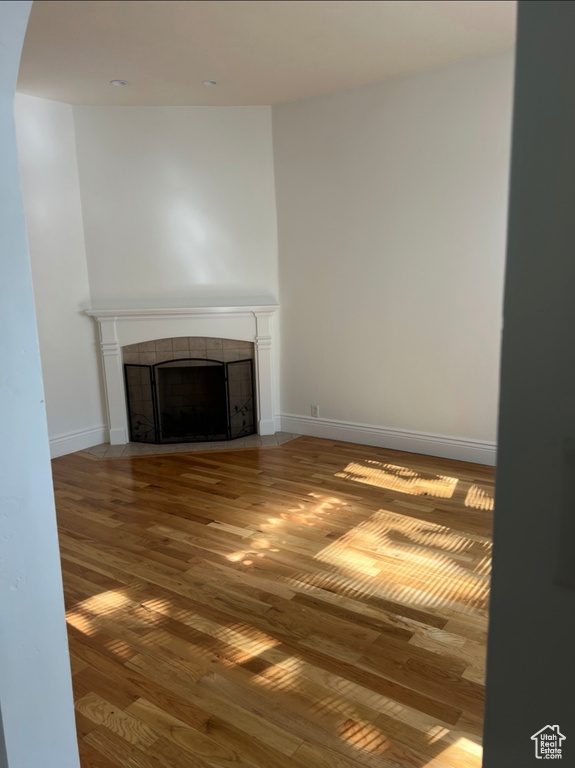 Unfurnished living room featuring a tiled fireplace, wood finished floors, baseboards, and arched walkways