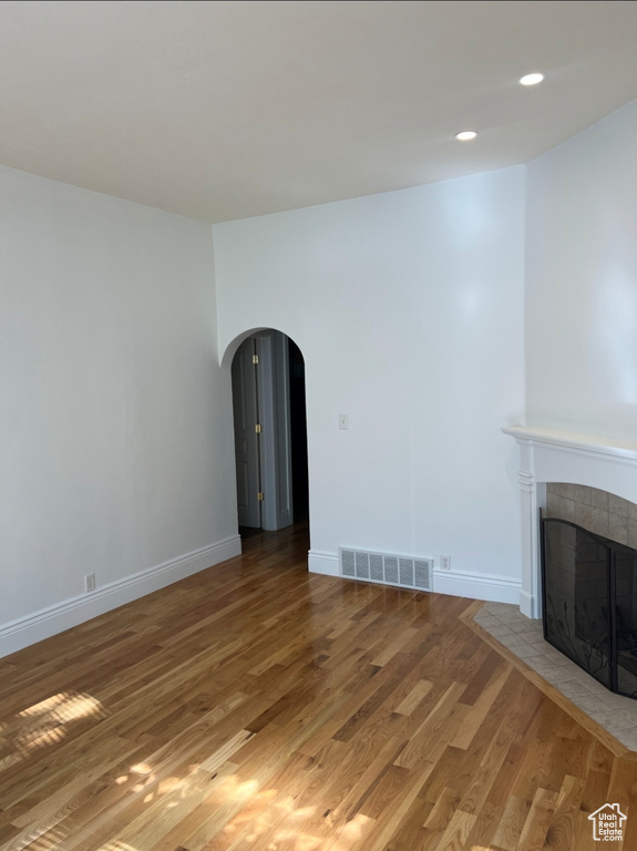Unfurnished living room featuring arched walkways, light wood-style floors, a fireplace, baseboards, and recessed lighting