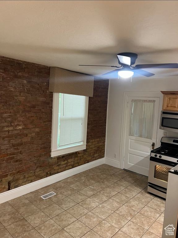 Kitchen featuring appliances with stainless steel finishes, baseboards, ceiling fan, brick wall, and light tile patterned floors
