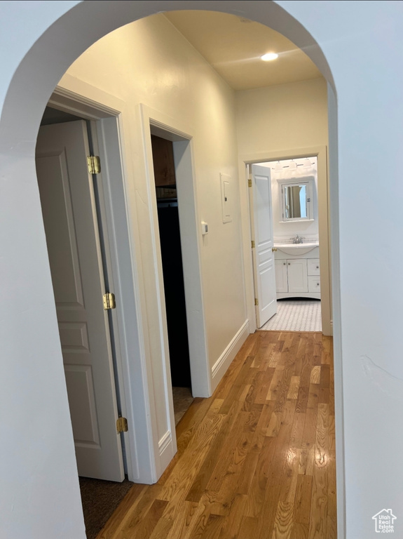 Hall with light wood finished floors, arched walkways, a sink, and baseboards