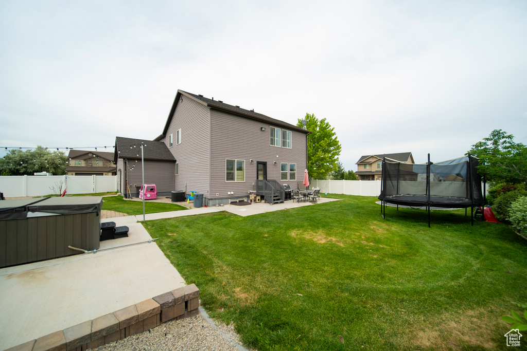 Rear view of property featuring a patio, a trampoline, and a hot tub