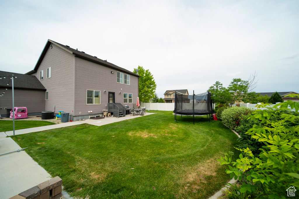 Back of house with a trampoline, a patio area, and cooling unit