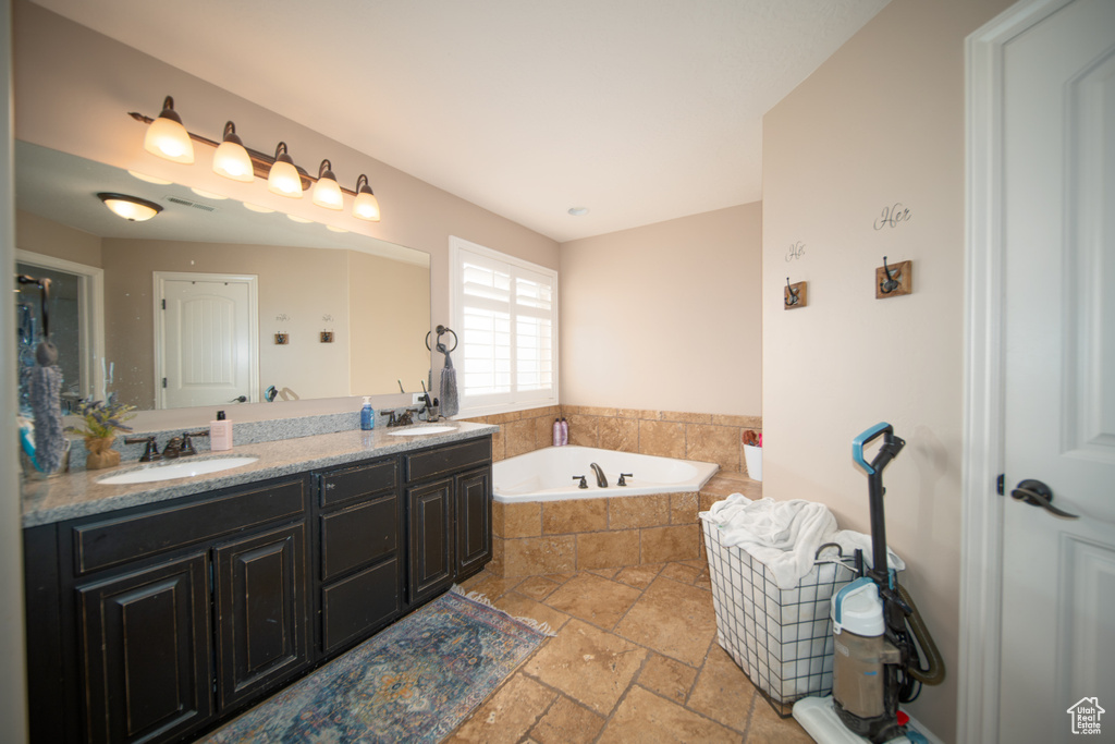 Bathroom with stone tile floors, a bath, and double vanity