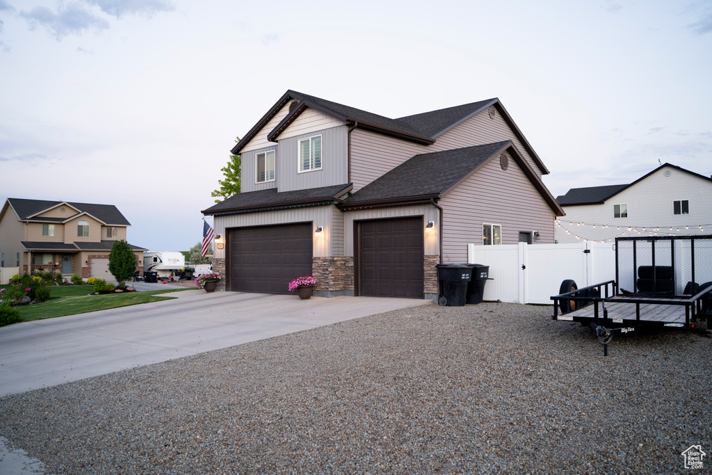 View of front of house with driveway, stone siding, a garage, and roof with shingles