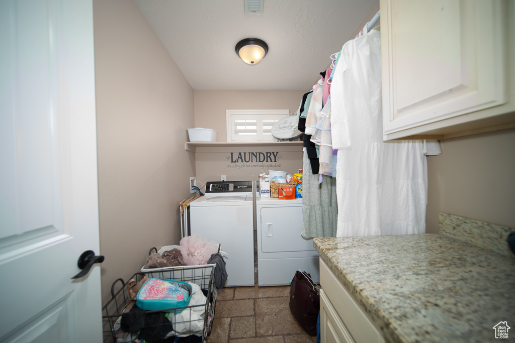 Laundry area featuring washing machine and clothes dryer, cabinet space, and stone tile floors
