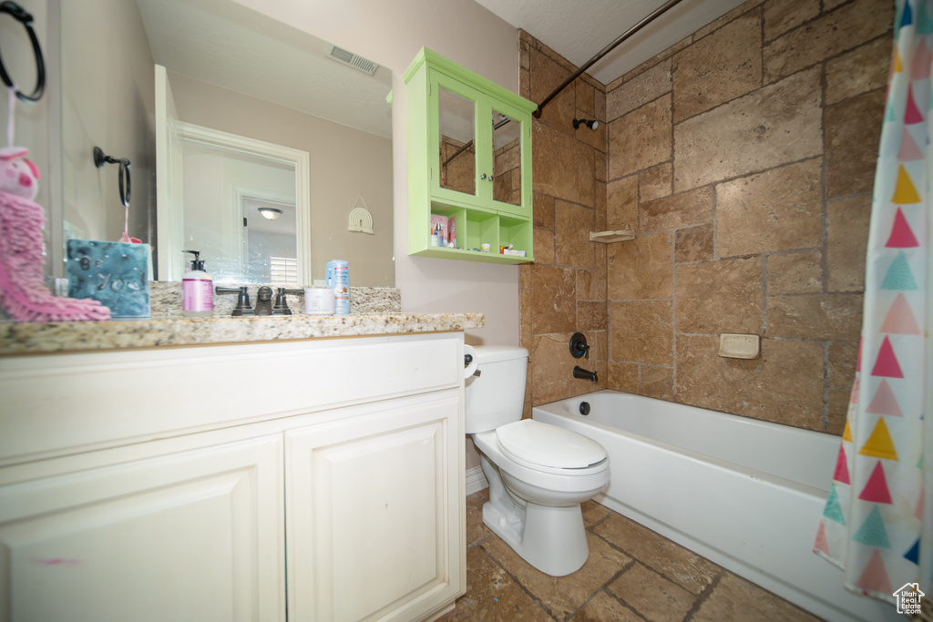 Bathroom with toilet, shower / tub combo with curtain, vanity, and stone tile flooring