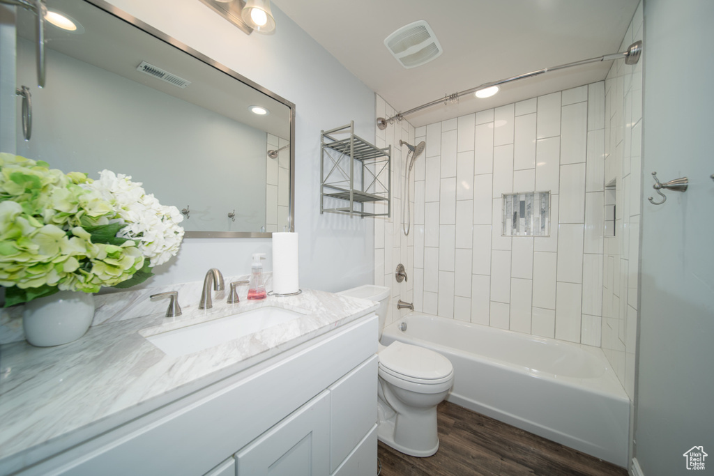 Full bathroom featuring wood finished floors, toilet, vanity, and washtub / shower combination