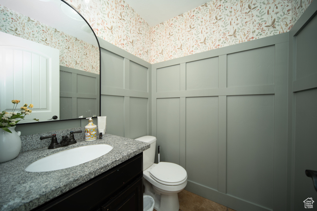 Half bathroom featuring a decorative wall, toilet, wallpapered walls, vanity, and a wainscoted wall