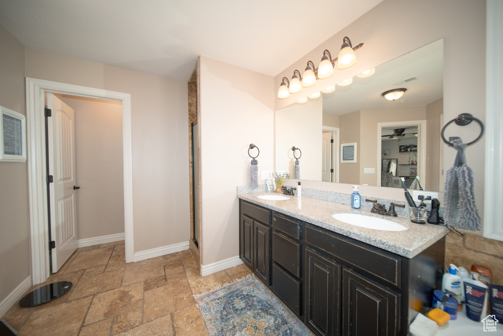 Full bathroom with stone tile floors, double vanity, baseboards, a ceiling fan, and an enclosed shower