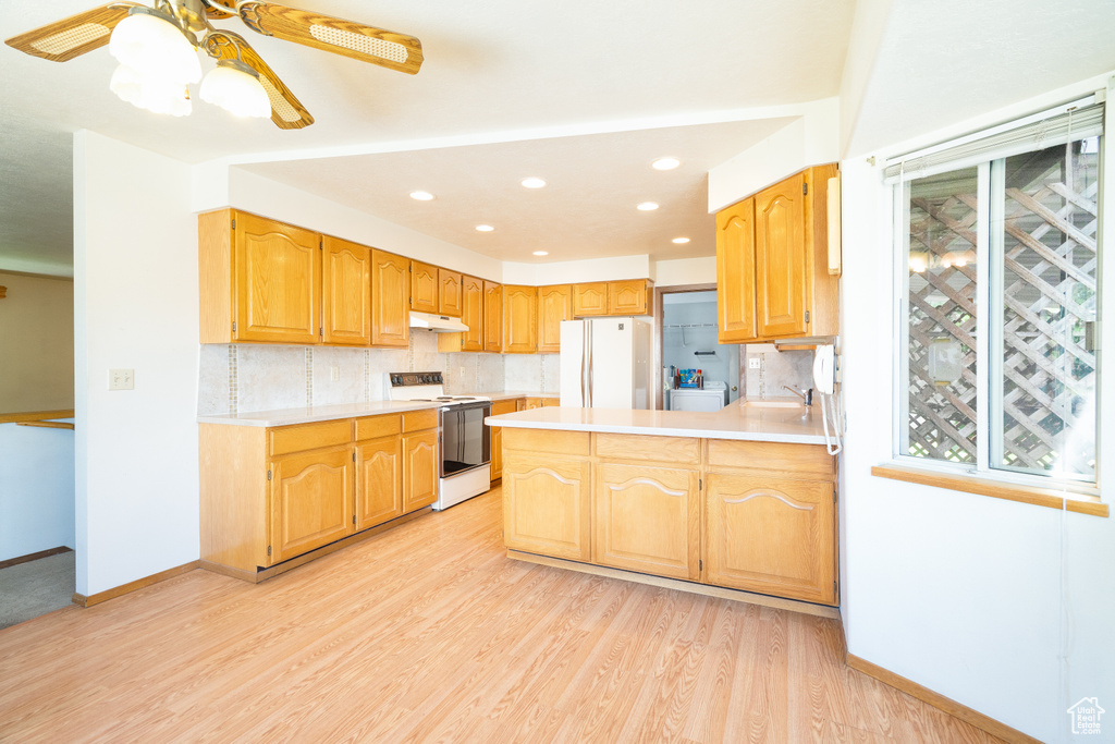 Kitchen featuring white appliances, light countertops, decorative backsplash, under cabinet range hood, and recessed lighting