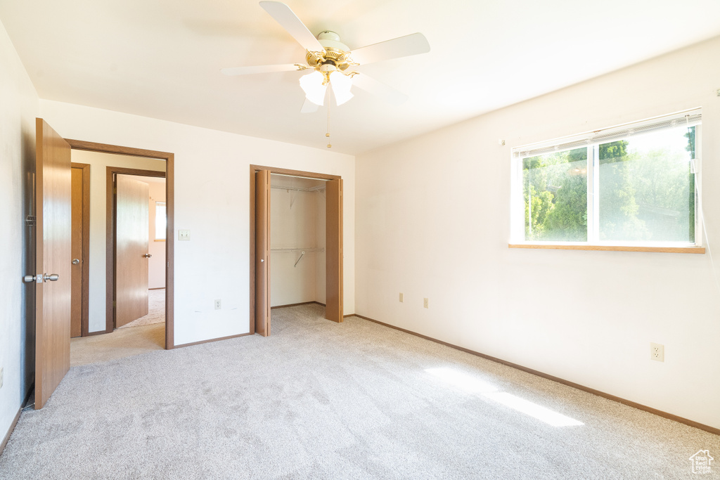 Unfurnished bedroom featuring light colored carpet, a closet, baseboards, and a ceiling fan