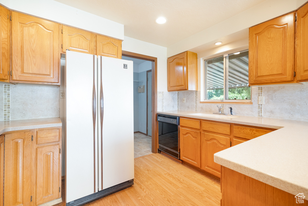 Kitchen with freestanding refrigerator, dishwasher, a sink, light wood finished floors, and light countertops
