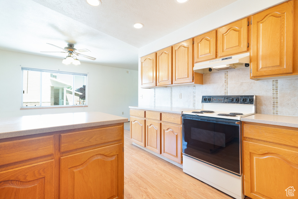Kitchen with range with electric cooktop, under cabinet range hood, light countertops, backsplash, and recessed lighting