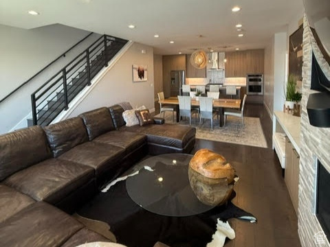 Living room featuring recessed lighting, dark wood-type flooring, stairway, and a stone fireplace