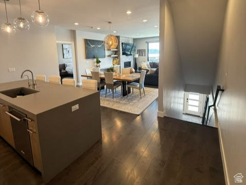 Kitchen featuring modern cabinets, a sink, dark wood-type flooring, hanging light fixtures, and an island with sink