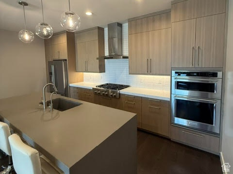 Kitchen with wall chimney exhaust hood, appliances with stainless steel finishes, a sink, modern cabinets, and recessed lighting