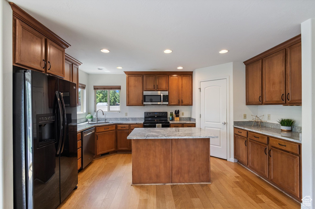 Kitchen with black appliances, light wood-type flooring, a kitchen island, recessed lighting, and brown cabinetry
