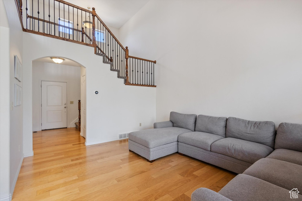 Living area featuring arched walkways, a towering ceiling, stairway, and light wood-style floors