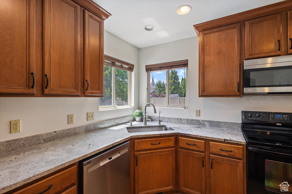 Kitchen featuring stainless steel appliances, brown cabinetry, recessed lighting, and light stone countertops