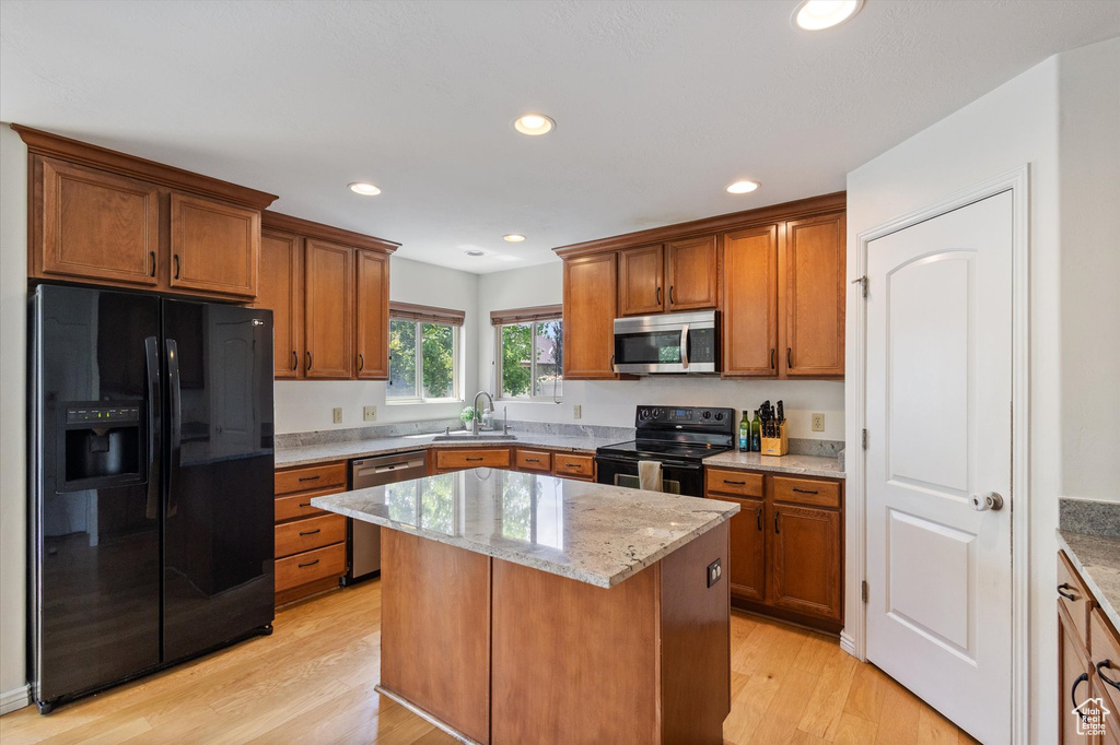 Kitchen with black appliances, brown cabinets, light stone counters, a kitchen island, and recessed lighting